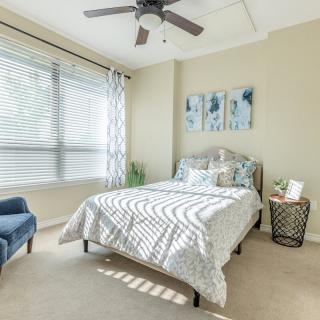 A bright and airy bedroom with a neatly made bed, large window, and tasteful decor.