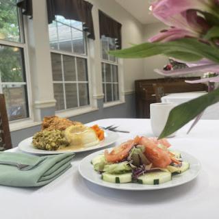 A beautifully arranged lunch featuring a fresh salad with cucumber and garnishes, complemented by a side dish, set in a well-lit dining area.