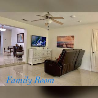 A cozy family room featuring a reclining sofa, ceiling fan, and a television set on a white cabinet.