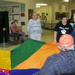 Residents participate in an indoor activity using a colorful parachute at a nursing home.