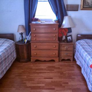 A cozy bedroom featuring twin beds, a wooden dresser, and natural light coming through the window.