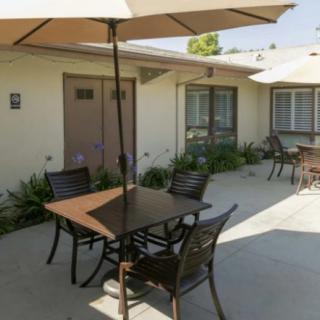 A sunny patio area with tables, chairs, and umbrellas outside a building.