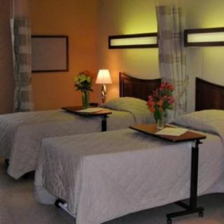 A hospital room with two neatly arranged beds, decorated with flowers and lit by a warm lamp.