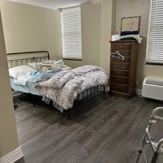 A cozy, unmade bedroom featuring a metal bed frame, a wooden dresser, and natural light from the window.