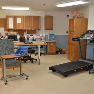 A physical therapy room equipped with a treadmill and various office furniture for rehabilitation activities.