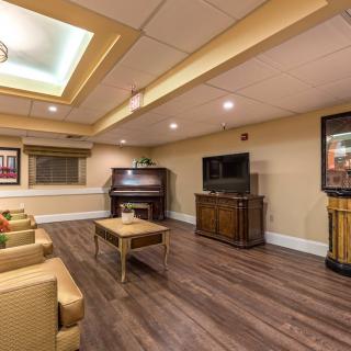 A cozy living room with a piano, television, and comfortable seating on wooden flooring.