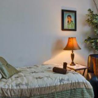 A cozy bedroom with a neatly made bed, a lamp on the side table, and wall art above.