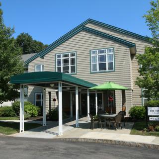 A residential building with a green awning and outdoor seating area surrounded by trees.