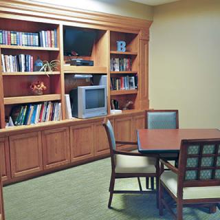 A cozy library room with a bookshelf, television, and a table with chairs.