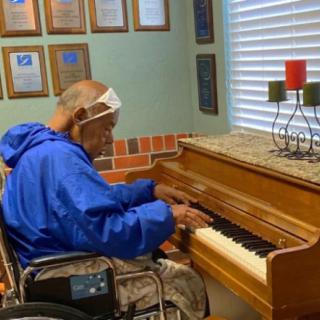 An elderly person in a wheelchair playing the piano in a decorated room.