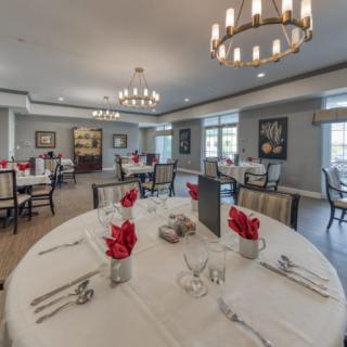An elegantly set dining room with round tables, decorated with red flowers and sophisticated table settings.