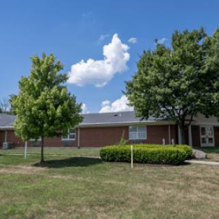 A residential building with a well-maintained lawn and trees under a bright blue sky.