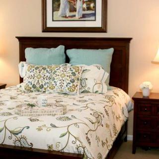 A cozy bedroom with a neatly made bed, decorative pillows, and matching nightstands with lamps.