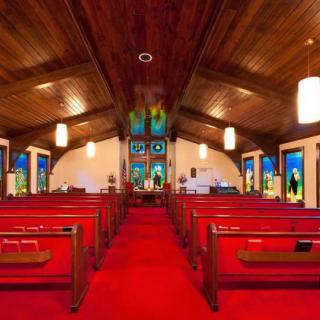A beautifully lit church interior featuring red carpeted aisles, wooden ceiling, and colorful stained glass windows.