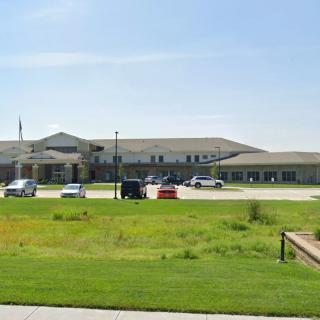 A school building with a large grassy lawn and a parking lot in front.