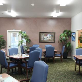 A neatly arranged dining area with blue chairs and tables, decorated with indoor plants and artwork on the walls.