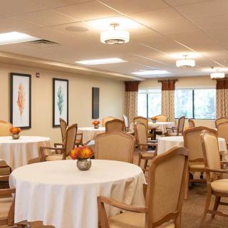 A well-lit dining room with round tables and chairs, decorated with framed art on the walls and natural light coming through the windows.