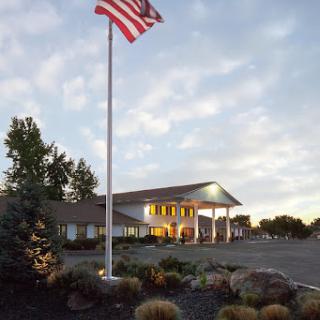 A welcoming building with an American flag flying in front, surrounded by trees and a clear sky.