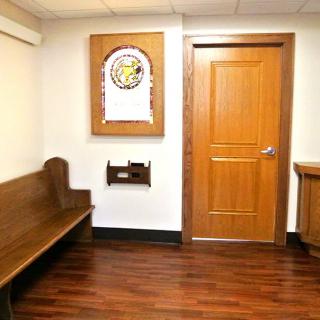 A waiting area with a wooden bench and door, featuring artwork on the wall.