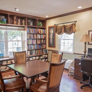 A cozy library room featuring wooden bookshelves, a table with chairs, and a computer by the window.
