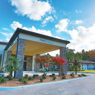 A modern building entrance with surrounding greenery under a partly cloudy sky.
