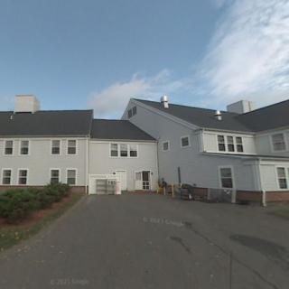 A residential building with a white exterior, featuring multiple windows and a driveway under a cloudy sky.