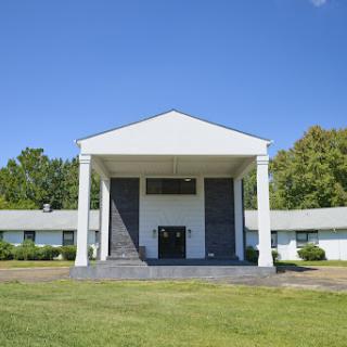 A modern building with a prominent front entrance, surrounded by lush greenery and under a clear blue sky.