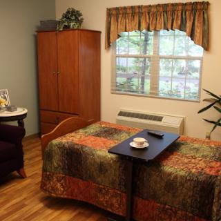 A cozy bedroom featuring a bed with a decorative comforter, a wooden wardrobe, and a small table by the window.