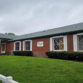 A brick building with multiple windows and green grass in front, set against an overcast sky.