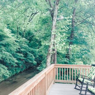 A tranquil view of a lush forest from a wooden deck with a rocking chair overlooking a gently flowing river.