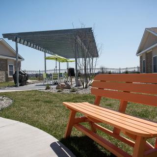 A sunny outdoor area featuring an orange bench, a pergola, and well-maintained green spaces.