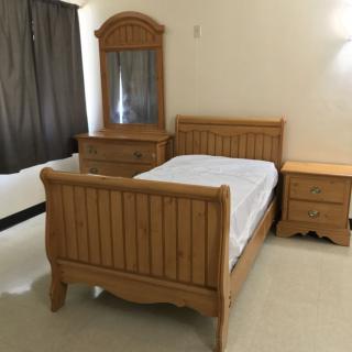 A simple bedroom with wooden furniture, including a bed, dresser with mirror, and nightstand.