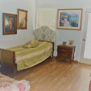 A cozy bedroom with a single bed, wooden floor, and decorative paintings on the wall.