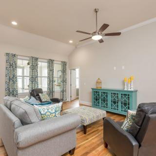 A cozy living room featuring comfortable sofas, a plush armchair, and a stylish coffee table on wood flooring, complemented by decorative pillows, curtains, and a ceiling fan.