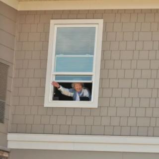 A person waving from inside a house through an open window.