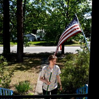 A woman walks towards her house with an American flag gently waving in the background.