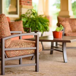 A cozy outdoor patio setup with cushioned chairs, a table, and potted plants.
