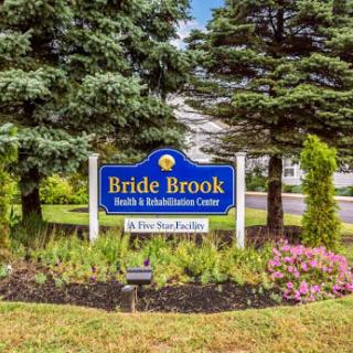 Welcome sign of Bride Brook Health & Rehabilitation Center, surrounded by a colorful garden.