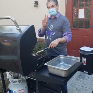 A person wearing a mask grilling food outdoors.