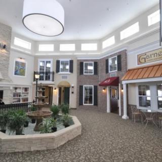 A bright indoor atrium featuring a small fountain and storefronts, designed to resemble an outdoor courtyard.