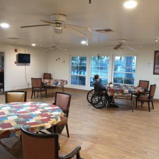A quiet dining area in a nursing home with tables, chairs, and a resident in a wheelchair.