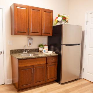 A compact kitchen area featuring wooden cabinets, a sink, and a stainless steel refrigerator.
