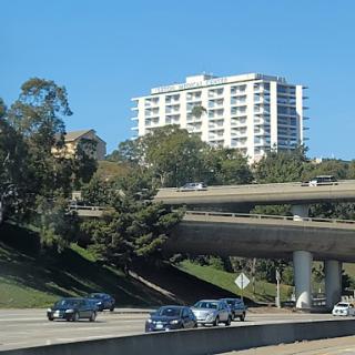 A view of a modern building situated above a busy highway, surrounded by greenery.