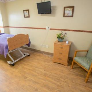 A clean and organized hospital room featuring a bed, a television on the wall, a chair, and a small bedside cabinet.