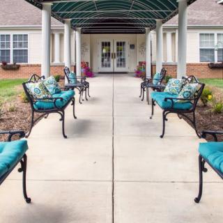 A covered walkway leading to a building entrance, lined with benches adorned with teal cushions.