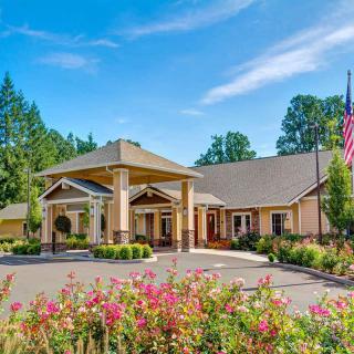 A beautiful building entrance surrounded by colorful flowers and greenery, with a clear blue sky in the background.