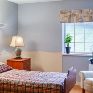 A cozy bedroom with a single bed, lamp on the nightstand, and a window with a plant.