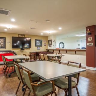 Cozy dining area with tables, chairs, and a television, complemented by a bar counter and framed pictures on the walls.