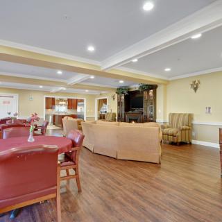 A spacious living room with comfortable seating and a large television, featuring hardwood floors and bright lighting.