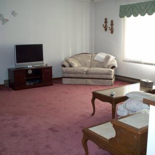 A spacious living room with a sofa, television, and wooden coffee tables on a pink carpet.